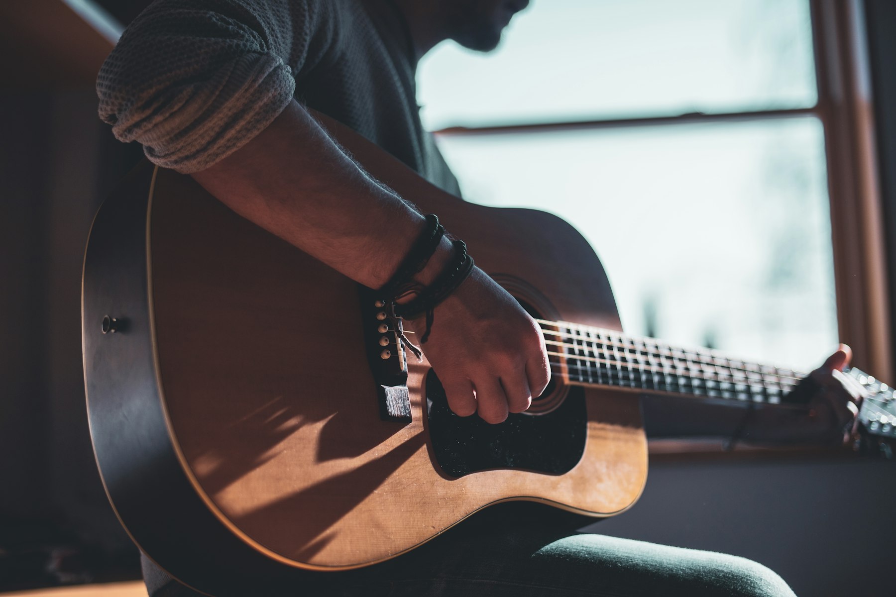 A person playing a sunburst acoustic guitar beside a bright window