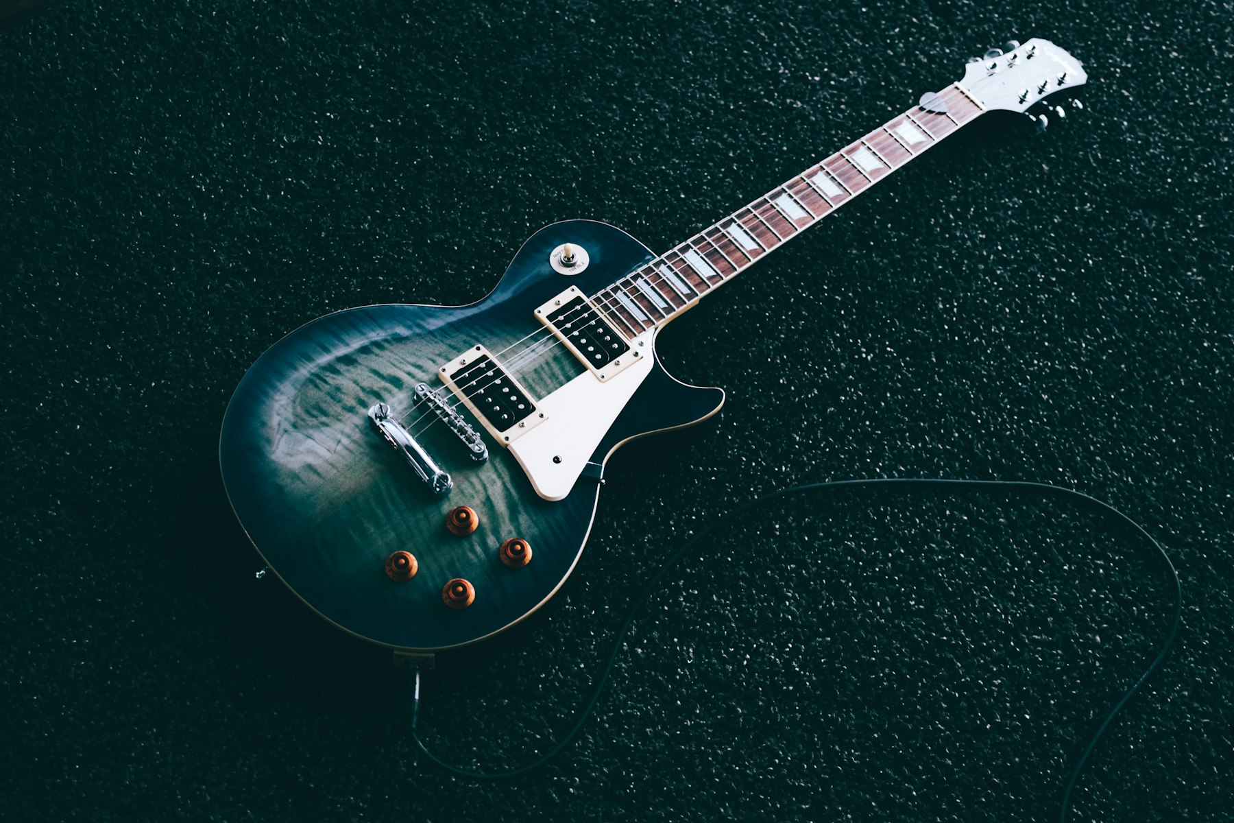 A sunburst electric guitar photographed from above on a dark textured floor