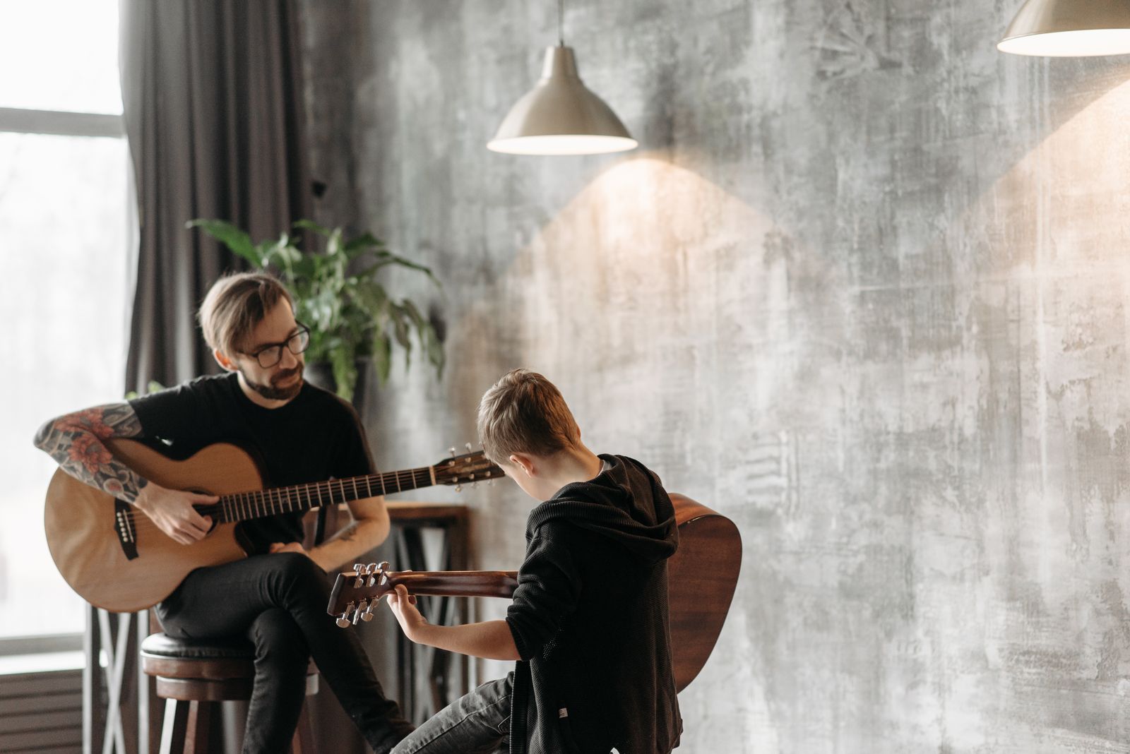 A guitar teacher and a young student sitting together with acoustic guitars