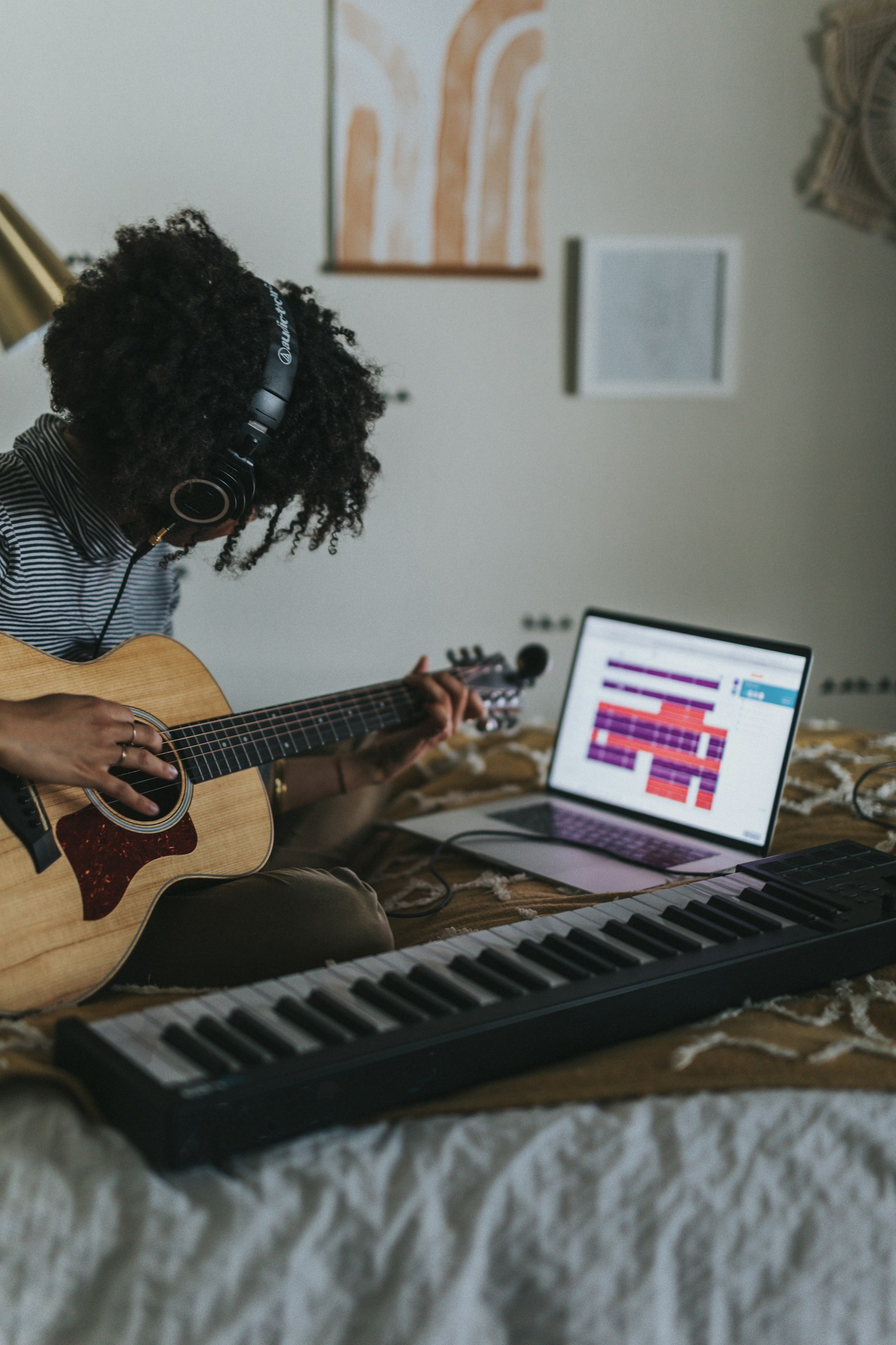 A student practising acoustic guitar at home with a laptop open for an online lesson