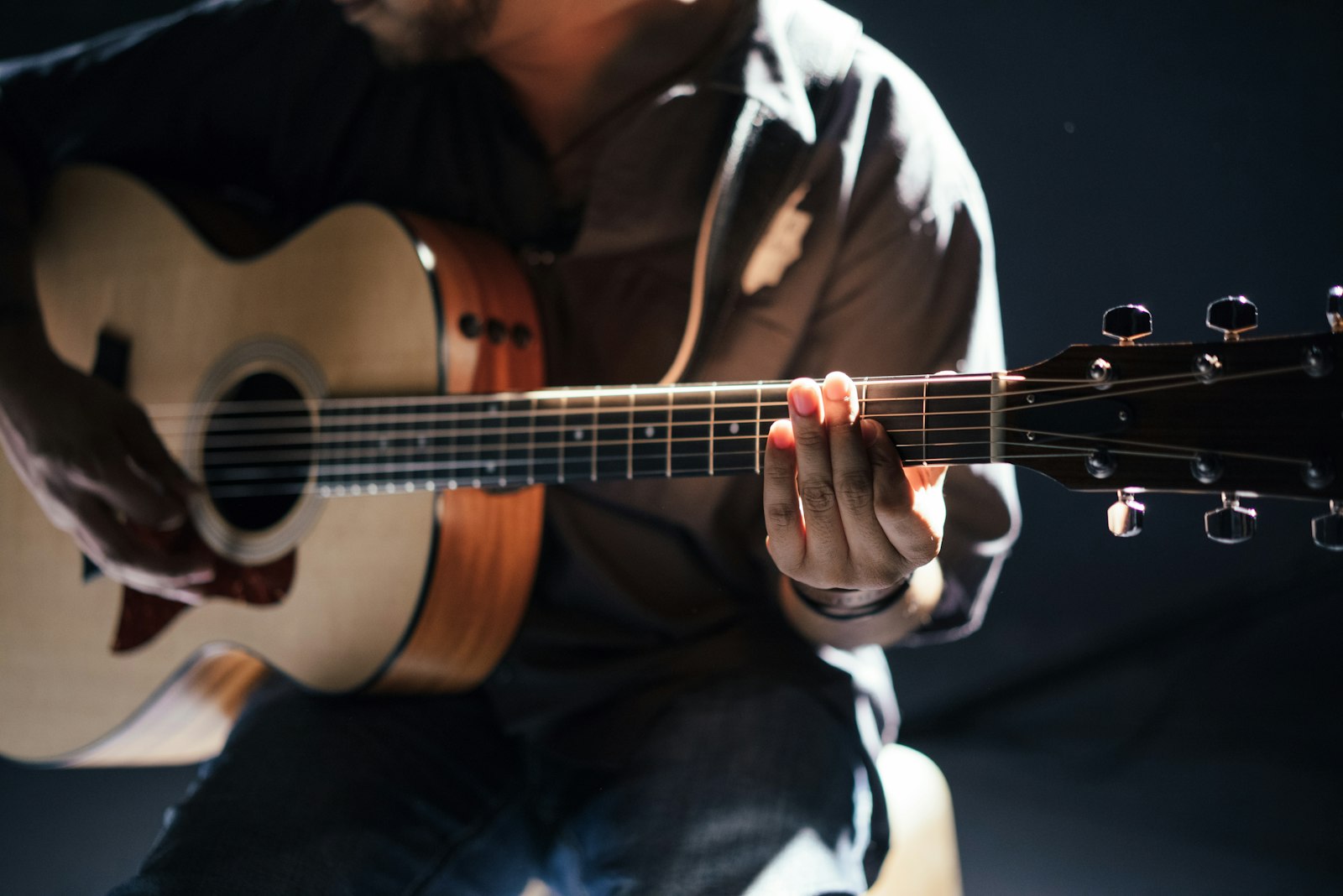 A guitarist seated with an acoustic guitar, captured in quiet studio light